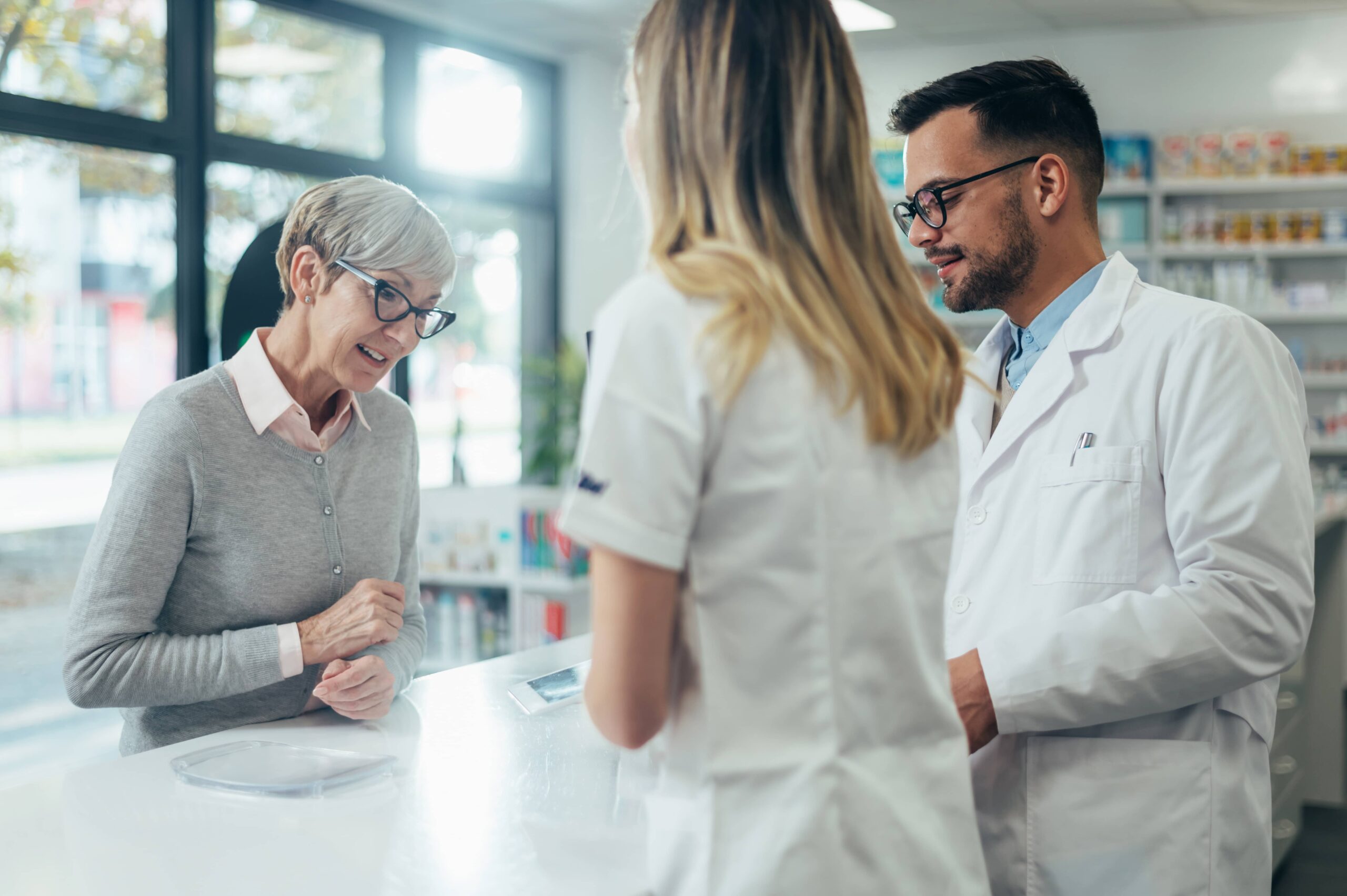Zwei Apotheker geben einer älteren Kundin in einer Apotheke verschreibungspflichtige Medikamente